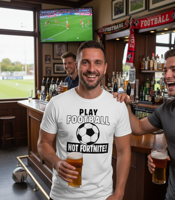 Man in a bar wearing a Cows Corner T-shirt with the funny football slogan on the front that reads'Play Football Not Fortnite!' t-shirt, holding a beer.  Cows Corner gifts are perfect for sport-mad fans, these gifts work brilliantly for birthdays, new baby celebrations, Father’s Day, Mother’s Day, Christmas, anniversaries, thank you gifts, end-of-season team awards, graduations, retirements, and just-because moments when you want to raise a smile. Designed for people who appreciate thoughtful gift