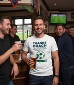 A group of men in a pub with one wearing a 'Thanks Coach' t-shirt, holding a beer. The man is wearing a Cows Corner t-shirt with the football slogan on the front that reads 'Thanks Coach From the First Touch to Final Whistle, You’ve Been the Heat of It All'. Cows Corner gifts are perfect for sport-mad fans, these gifts work brilliantly for birthdays, new baby celebrations, Father’s Day, Mother’s Day, Christmas, anniversaries, thank you gifts, end-of-season team awards, graduations, retirements