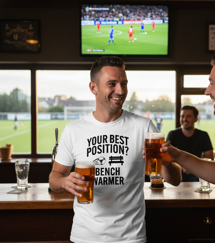 Two men in a bar holding beers, one wearing a white t-shirt with a humorous print, TV showing a sports match in the background.  The man is wearing a Cows Corner T-shirt with the funny football slogan on the front that reads 'Your Best Position? Bench Warmer'.  Cows Corner gifts are perfect for sport-mad fans, these gifts work brilliantly for birthdays, new baby celebrations, Father’s Day, Mother’s Day, Christmas, anniversaries, thank you gifts, end-of-season team awards, graduations, retirements, 