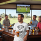 Group of men in a bar watching golf on TV and drinking beer. The man is wearing a Cows Corner t-shirt with the funny golf slogan 'Hole-In-One Today… Pub Stories Forever'. Cows Corner gifts are perfect for sport-mad fans, these gifts work brilliantly for birthdays, new baby celebrations, Father’s Day, Mother’s Day, Christmas, anniversaries, thank you gifts, end-of-season team awards, graduations, retirements, and just-because moments when you want to raise a smile. 
