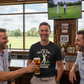 Three men in a bar watching a golf game on TV, one holding a beer. The man is wearing a Cows Corner t-shirt with a funny golf slogan on the front 'I Got A Hole-In-One… My Mates Got Trauma'. Cows Corner gifts are perfect for sport-mad fans, these gifts work brilliantly for birthdays, new baby celebrations, Father’s Day, Mother’s Day, Christmas, anniversaries, thank you gifts, end-of-season team awards, graduations, retirements, and just-because moments when you want to raise a smile. 
