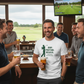 Group of men in a bar watching golf on TV and drinking beer. The man is wearing a Cows Corner t-shirt with the golf coach slogan on the front that reads 'Grip, Posture, Believe. Thank You for Everything Coach'. Cows Corner gifts are perfect for sport-mad fans, these gifts work brilliantly for birthdays, new baby celebrations, Father’s Day, Mother’s Day, Christmas, anniversaries, thank you gifts, end-of-season team awards, graduations, retirements, and just-because moments when you want to raise a smile.