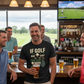Group of men in a bar with one wearing a Cows Corner t-shirt with a funny golf slogan on the front that reads 'If Golf Was Easy You'd Be Good At It'. Cows Corner gifts are perfect for sport-mad fans, these gifts work brilliantly for birthdays, new baby celebrations, Father’s Day, Mother’s Day, Christmas, anniversaries, thank you gifts, end-of-season team awards, graduations, retirements, and just-because moments when you want to raise a smile. Designed for people who appreciate thoughtful gift