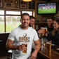Man in a pub wearing a 'Rugby Because Punching' t-shirt, holding a beer with friends around him. The man is wearing a Cows Corner t-shirt with a funny rugby slogan on the front that reads 'Rugby Because Punching People in Public Is Frowned Upon'. Cows Corner gifts are perfect for sport-mad fans, these gifts work brilliantly for birthdays, new baby celebrations, Father’s Day, Mother’s Day, Christmas, anniversaries, thank you gifts, end-of-season team awards, graduations, retirements, and just-because moments