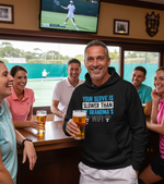 Man in a bar wearing a hoodie with a humorous message, holding a beer, surrounded by friends watching tennis on TV. The man is wearing a Cows Corner hoodie with the funny tennis slogan 'Your Serve Is Slower Than My Grandma's Wifi'.  Cows Corner gifts are perfect for sport-mad fans, these gifts work brilliantly for birthdays, new baby celebrations, Father’s Day, Mother’s Day, Christmas, anniversaries, thank you gifts, end-of-season team awards, graduations, retirements, and just-because moments 