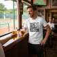 Man in a sports bar holding beers, wearing a t-shirt with tennis-themed text. The man is wearing a Cows Corner t-shirt with the tennis coach slogan on the front that reads 'Thanks for the Love the Lobs and the Lessons. Best Tennis Coach Ever'. Cows Corner gifts are perfect for sport-mad fans, these gifts work brilliantly for birthdays, new baby celebrations, Father’s Day, Mother’s Day, Christmas, anniversaries, thank you gifts, end-of-season team awards, graduations, retirements, and just-because moments