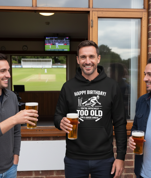 Three men standing outside a building with a TV screen showing a sports game, holding beer glasses. The man is wearing a Cows Corner hoodie with the funny cricket birthday slogan 'Happy Birthday! You’re Officially Too Old for a Quick Single'.  Cows Corner gifts are perfect for sport-mad fans, these gifts work brilliantly for birthdays, new baby celebrations, Father’s Day, Mother’s Day, Christmas, anniversaries, thank you gifts, end-of-season team awards, graduations, retirements, and just-because moments