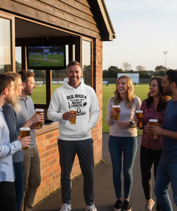 Group of people enjoying drinks outside a pub with a television screen displaying a sports match. The man is wearing a Cows Corner hoodie with the funny cricket birthday slogan 'Old, Bold & Still Looking for a Decent Length. Happy Birthday'. Cows Corner gifts are perfect for sport-mad fans, these gifts work brilliantly for birthdays, new baby celebrations, Father’s Day, Mother’s Day, Christmas, anniversaries, thank you gifts, end-of-season team awards, graduations, retirements, and just-because moments
