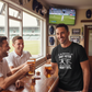 Three men in a pub watching a sports game on TV, one wearing a humorous t-shirt. A man wearing a Cows Corner t-shirt with the funny cricket birthday slogan 'You Used to be a Heavy Hitter. Now you’ve Just Got Heavy Tits.' Cows Corner gifts are perfect for sport-mad fans, these gifts work brilliantly for birthdays, new baby celebrations, Father’s Day, Mother’s Day, Christmas, anniversaries, thank you gifts, end-of-season team awards, graduations, retirements, and just-because moments 