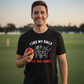 Man wearing a black t-shirt with a graphic and text, holding a red ball on a grassy field. The man is wearing a Cows Corner t-shirt with the funny cricket slogan 'I Like My Balls Red And Hard'. Cows Corner gifts are perfect for sport-mad fans, these gifts work brilliantly for birthdays, new baby celebrations, Father’s Day, Mother’s Day, Christmas, anniversaries, thank you gifts, end-of-season team awards, graduations, retirements, and just-because moments when you want to raise a smile. 
