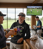 Two men enjoying drinks in a bar with a television showing a golf game. The man is wearing a Cows Corner hoodie with a funny golf slogan 'Your Swing Looks Like a Drunk Octopus Falling out of a Tree'. Cows Corner gifts are perfect for sport-mad fans, these gifts work brilliantly for birthdays, new baby celebrations, Father’s Day, Mother’s Day, Christmas, anniversaries, thank you gifts, end-of-season team awards, graduations, retirements, and just-because moments when you want to raise a smile. 
