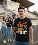 Person wearing a black t-shirt with humorous fantasy football text, standing outdoors with friends in the background. A Cows Corner t-shirt with the funny football slogan 'Fantasy Football Is Just Me Getting F*cked Over Weekly'. Cows Corner gifts are perfect for sport-mad fans, these gifts work brilliantly for birthdays, new baby celebrations, Father’s Day, Mother’s Day, Christmas, anniversaries, thank you gifts, end-of-season team awards, graduations, retirements, and just-because moments