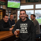 Man in a bar wearing a hoodie with humorous text, holding a beer, with a TV showing a sports game in the background. The man is wearing a Cows Corner hoodie with the funny fantasy football slogan on the front that reads 'I Bench Goals and Start W*nkers'. Cows Corner gifts are perfect for sport-mad fans, these gifts work brilliantly for birthdays, new baby celebrations, Father’s Day, Mother’s Day, Christmas, anniversaries, thank you gifts, end-of-season team awards, graduations, retirements, and just-because