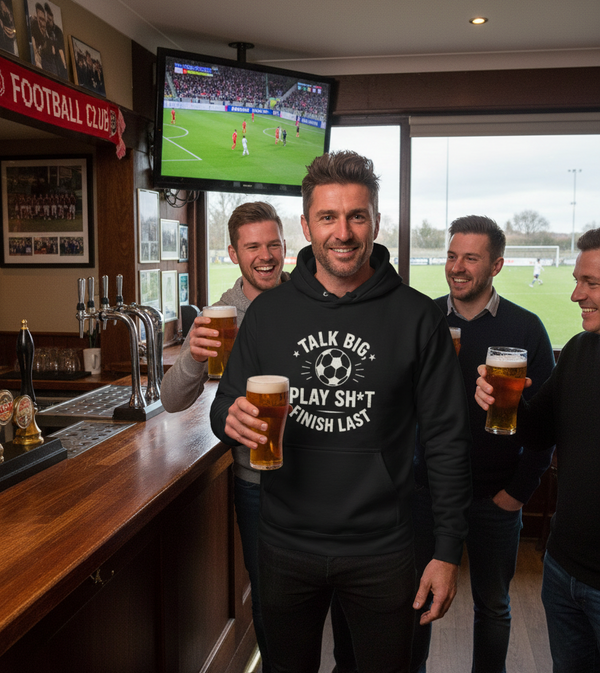 People in a pub watching a football match on TV, with one person holding a beer and wearing a hoodie with text. The man is wearing a Cows Corner hoodie with the funny fantasy football slogan on the front that reads 'Talk Big, Play Sh*t, Finish Last'. Cows Corner gifts are perfect for sport-mad fans, these gifts work brilliantly for birthdays, new baby celebrations, Father’s Day, Mother’s Day, Christmas, anniversaries, thank you gifts, end-of-season team awards, graduations, retirements, and just-because