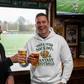 Man wearing a hoodie with humorous fantasy football text, holding beer glasses in a pub setting with sports memorabilia. The man is wearing a Cows Corner hoodie with the funny fantasy football slogan on the front that reads 'You're Utter Dogsh*t at Fantasy Football'.  Cows Corner gifts are perfect for sport-mad fans, these gifts work brilliantly for birthdays, new baby celebrations, Father’s Day, Mother’s Day, Christmas, anniversaries, thank you gifts, end-of-season team awards, graduations, retirements