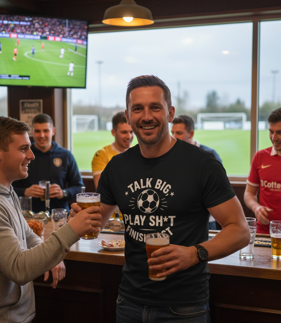 Man in a bar holding a beer with others, watching sports on TV. Man wearing a Cows Corner t-shirt with the funny fantasy football slogan on the front that reads 'Talk Big, Play Sh*t, Finish Last'.  Cows Corner gifts are perfect for sport-mad fans, these gifts work brilliantly for birthdays, new baby celebrations, Father’s Day, Mother’s Day, Christmas, anniversaries, thank you gifts, end-of-season team awards, graduations, retirements, and just-because moments when you want to raise a smile. 