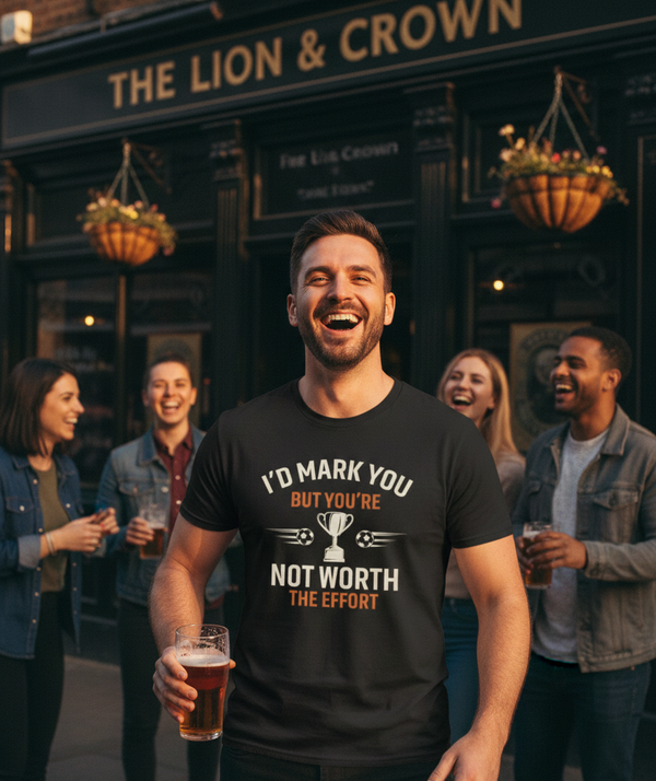 Man holding a beer in front of a pub with friends, wearing a t-shirt with humorous text. The man is wearing a Cows Corner t-shirt with the funny football slogan 'I’d Mark You but You’re Not Worth the Effort.' Cows Corner gifts are perfect for sport-mad fans, these gifts work brilliantly for birthdays, new baby celebrations, Father’s Day, Mother’s Day, Christmas, anniversaries, thank you gifts, end-of-season team awards, graduations, retirements, and just-because moments when you want to raise a smile. 

