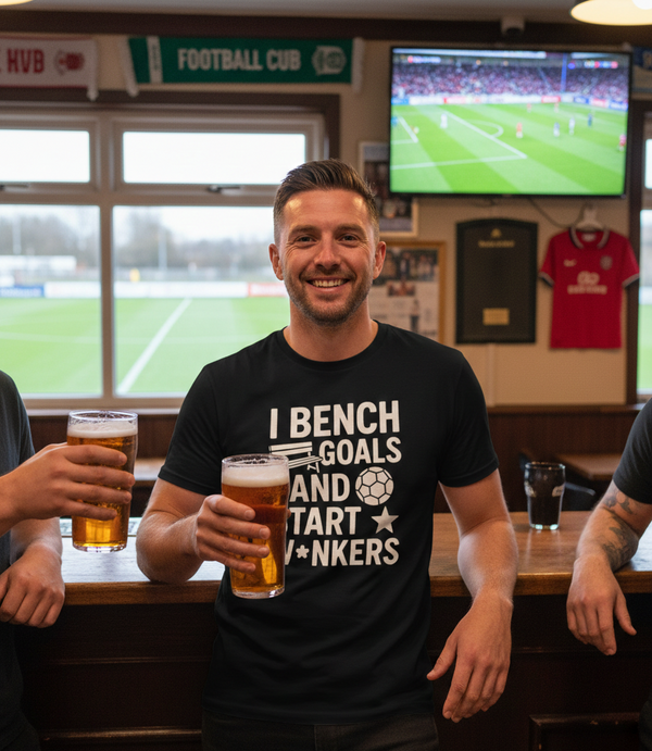 Man holding a beer in a pub with a TV showing a football match in the background. The man is wearing a Cows Corner t-shirt with the funny fantasy football slogan on the front that reads 'I Bench Goals and Start W*nkers'. Cows Corner gifts are perfect for sport-mad fans, these gifts work brilliantly for birthdays, new baby celebrations, Father’s Day, Mother’s Day, Christmas, anniversaries, thank you gifts, end-of-season team awards, graduations, retirements, and just-because moments 