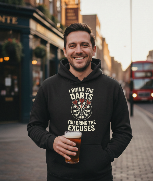 Man wearing a hoodie with a dartboard design and text, holding a beer in an urban setting. The man is wearing a Cows Corner hoodie with a funny darts slogan 'I Bring the Darts You Bring the Excuses'. Cows Corner gifts are perfect for sport-mad fans, these gifts work brilliantly for birthdays, new baby celebrations, Father’s Day, Mother’s Day, Christmas, anniversaries, thank you gifts, end-of-season team awards, graduations, retirements, and just-because moments when you want to raise a smile. 

