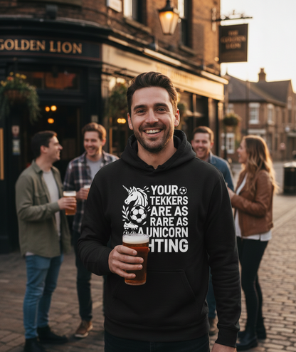Man wearing a hoodie with a humorous design, standing in a pub courtyard with others. The man is wearing a Cows Corner hoodie with a funny football slogan 'Your Tekkers Are As Rare as a Unicorn Sighting'. Cows Corner gifts are perfect for sport-mad fans, these gifts work brilliantly for birthdays, new baby celebrations, Father’s Day, Mother’s Day, Christmas, anniversaries, thank you gifts, end-of-season team awards, graduations, retirements, and just-because moments when you want to raise a smile. 

