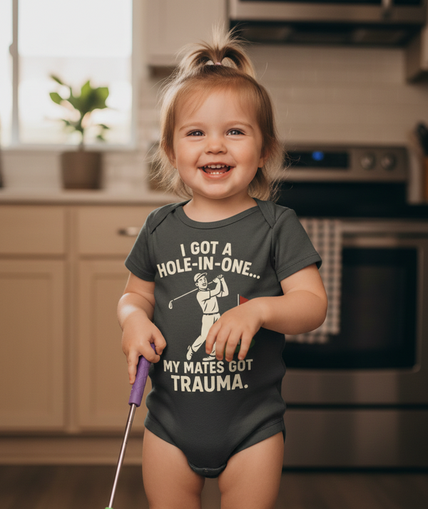Child wearing a humorous shirt with a golf graphic and text in a kitchen. The baby is wearing a Cows Corner baby grow with funny golf slogan 'I Got A Hole-In-One… My Mates Got Trauma'. Cows Corner gifts are perfect for sport-mad fans, these gifts work brilliantly for birthdays, new baby celebrations, Father’s Day, Mother’s Day, Christmas, anniversaries, thank you gifts, end-of-season team awards, graduations, retirements, and just-because moments when you want to raise a smile. 
