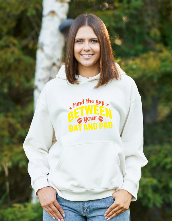 A lady wearing a white hoodie with Mind the Gap Between Your Bat and Pad on the front. A Funny Cricket Hoodie, Premium Fabric, Multiple Adult Sizes