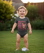 A baby is wearing a Cows Corner baby grow with a funny rugby slogan 'Mum Rucks, Mum Tackles, Mum Wins at Life!'. Cows Corner gifts are perfect for sport-mad fans, these gifts work brilliantly for birthdays, new baby celebrations, Father’s Day, Mother’s Day, Christmas, anniversaries, thank you gifts, end-of-season team awards, graduations, retirements, and just-because moments when you want to raise a smile. 

