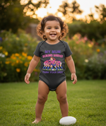 Child wearing a humorous onesie in a garden. The baby is wearing a Cows Corner baby grow with a funny rugby slogan 'My Mum Scrums Harder Than Your Dad!'. Cows Corner gifts are perfect for sport-mad fans, these gifts work brilliantly for birthdays, new baby celebrations, Father’s Day, Mother’s Day, Christmas, anniversaries, thank you gifts, end-of-season team awards, graduations, retirements, and just-because moments when you want to raise a smile. 
