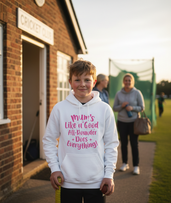 Child wearing a white hoodie with pink text, standing in front of a brick building.  The boy is wearing a Cows Corner hoodie with a funny cricket slogan 'Mums Like A Good All-rounder, Does Everything'. Cows Corner gifts are perfect for sport-mad fans, these gifts work brilliantly for birthdays, new baby celebrations, Father’s Day, Mother’s Day, Christmas, anniversaries, thank you gifts, end-of-season team awards, graduations, retirements, and just-because moments when you want to raise a smile. 
