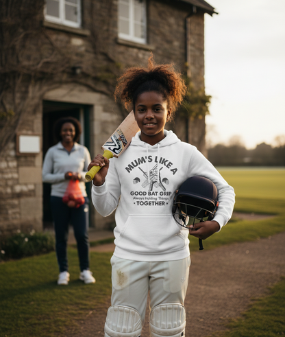 Person in white hoodie holding cricket equipment outdoors with another person in the background. The girl is wearing a Cows Corner hoodie with a funny cricket slogan 'Mums Like A Good Bat Grip, Always Holding Things Together'. Cows Corner gifts are perfect for sport-mad fans, these gifts work brilliantly for birthdays, new baby celebrations, Father’s Day, Mother’s Day, Christmas, anniversaries, thank you gifts, end-of-season team awards, graduations, retirements, and just-because moments 