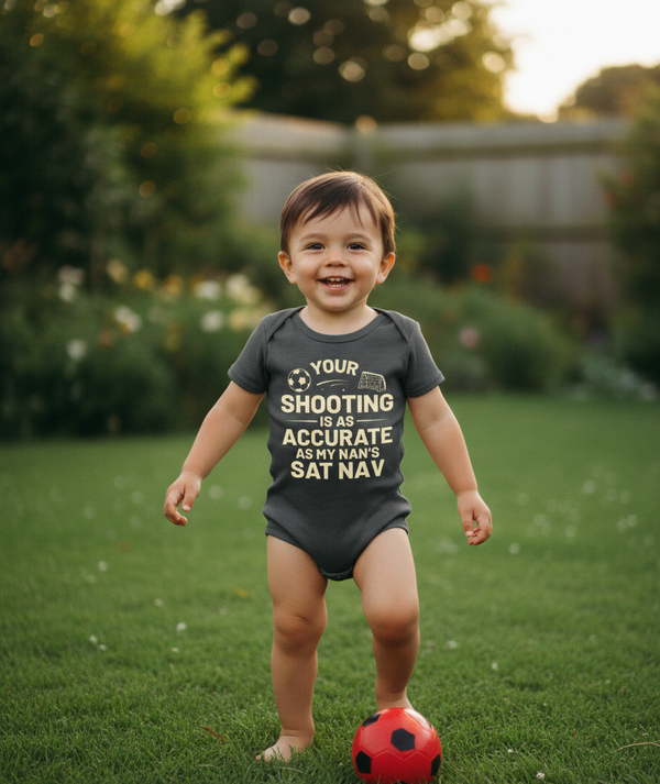 Child wearing a humorous onesie standing on grass with a soccer ball. The baby is wearing a Cows Corner baby grow with a funny football slogan 'Your Shooting Is As Accurate as My Nan’s Sat Nav'. Cows Corner gifts are perfect for sport-mad fans, these gifts work brilliantly for birthdays, new baby celebrations, Father’s Day, Mother’s Day, Christmas, anniversaries, thank you gifts, end-of-season team awards, graduations, retirements, and just-because moments when you want to raise a smile. 
