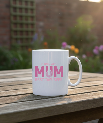 White mug with pink text on a wooden table outdoors. This is a Cows Corner mug with a funny tennis slogan 'Tennis with Mums. Best. Day. Ever!'. Cows Corner gifts are perfect for sport-mad fans, these gifts work brilliantly for birthdays, new baby celebrations, Father’s Day, Mother’s Day, Christmas, anniversaries, thank you gifts, end-of-season team awards, graduations, retirements, and just-because moments when you want to raise a smile. 
