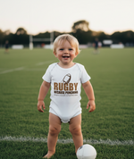 Child wearing a Cows Corner baby grow with a funny rugby slogan 'Rugby Because Punching People in Public Is Frowned Upon'. Cows Corner gifts are perfect for sport-mad fans, these gifts work brilliantly for birthdays, new baby celebrations, Father’s Day, Mother’s Day, Christmas, anniversaries, thank you gifts, end-of-season team awards, graduations, retirements, and just-because moments when you want to raise a smile. 
