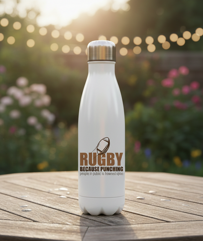 White water bottle with rugby design and text on a wooden surface with a blurred garden background. This is a Cows Corner water bottle with the funny rugby slogan 'Rugby Because Punching People in Public Is Frowned Upon'.  Cows Corner gifts are perfect for sport-mad fans, these gifts work brilliantly for birthdays, new baby celebrations, Father’s Day, Mother’s Day, Christmas, anniversaries, thank you gifts, end-of-season team awards, graduations, retirements, and just-because moments 