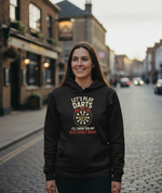 Woman wearing a black hoodie with a dart design and text on a street. The lady is wearing a Cows Corner hoodie with the funny darts slogan 'Lets Play Darts I'll Show You My Best Shaft Work'. Cows Corner gifts are perfect for sport-mad fans, these gifts work brilliantly for birthdays, new baby celebrations, Father’s Day, Mother’s Day, Christmas, anniversaries, thank you gifts, end-of-season team awards, graduations, retirements, and just-because moments when you want to raise a smile. 
