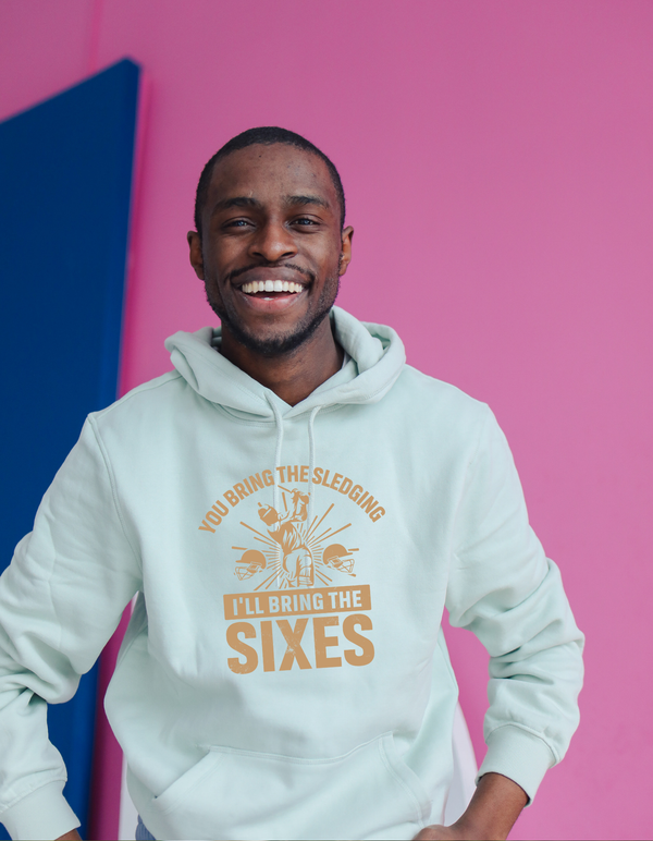A man wearing a white hoodie with You Bring the Sledging, I'll Bring the Sixes on the front. A Funny Cricket Hoodie, Premium Fabric, Multiple Adult Sizes