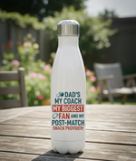 White water bottle with colorful text on a wooden table outdoors. This is a Cows Corner water bottle with a funny rugby slogan 'Dad’s My Coach My Biggest Fan and My Post-Match Snack Provider!'. Cows Corner gifts are perfect for sport-mad fans, these gifts work brilliantly for birthdays, new baby celebrations, Father’s Day, Mother’s Day, Christmas, anniversaries, thank you gifts, end-of-season team awards, graduations, retirements, and just-because moments when you want to raise a smile. 
