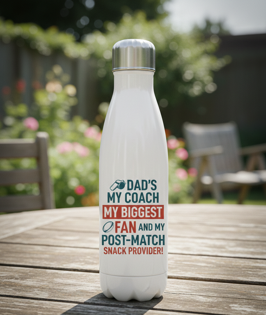 White water bottle with colorful text on a wooden table outdoors. This is a Cows Corner water bottle with a funny rugby slogan 'Dad’s My Coach My Biggest Fan and My Post-Match Snack Provider!'. Cows Corner gifts are perfect for sport-mad fans, these gifts work brilliantly for birthdays, new baby celebrations, Father’s Day, Mother’s Day, Christmas, anniversaries, thank you gifts, end-of-season team awards, graduations, retirements, and just-because moments when you want to raise a smile. 
