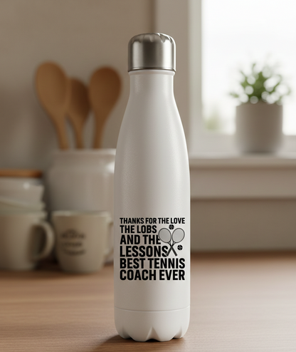 White insulated bottle with text on a kitchen counter. This is a Cows Corner water bottle with a funny tennis slogan 'Thanks for the Love the Lobs and the Lessons. Best Tennis Coach Ever'. Cows Corner gifts are perfect for sport-mad fans, these gifts work brilliantly for birthdays, new baby celebrations, Father’s Day, Mother’s Day, Christmas, anniversaries, thank you gifts, end-of-season team awards, graduations, retirements, and just-because moments when you want to raise a smile. 
