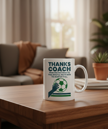 Mug with 'Thanks Coach' design on a wooden table in a cozy living room. This is a Cows Corner mug with a funny football slogan 'Thanks Coach From the First Touch to Final Whistle, You’ve Been the Heat of It All'. Cows Corner gifts are perfect for sport-mad fans, these gifts work brilliantly for birthdays, new baby celebrations, Father’s Day, Mother’s Day, Christmas, anniversaries, thank you gifts, end-of-season team awards, graduations, retirements, and just-because moments when you want to raise a smile. 
