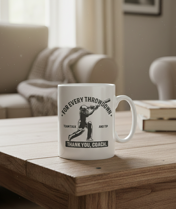 White mug with black text and graphics on a wooden table in a cozy living room. This is a Cows Corner mug with a funny cricket slogan 'For every throwdown, team talk and tip, thank you coach'. Cows Corner gifts are perfect for sport-mad fans, these gifts work brilliantly for birthdays, new baby celebrations, Father’s Day, Mother’s Day, Christmas, anniversaries, thank you gifts, end-of-season team awards, graduations, retirements, and just-because moments when you want to raise a smile. 
