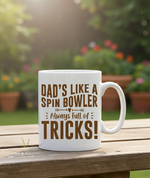 White mug with brown text on a wooden table outdoors. This is a Cows Corner mug with a funny cricket slogan 'Dad’s Like a Spin Bowler, Always Full of Tricks!'. Cows Corner gifts are perfect for sport-mad fans, these gifts work brilliantly for birthdays, new baby celebrations, Father’s Day, Mother’s Day, Christmas, anniversaries, thank you gifts, end-of-season team awards, graduations, retirements, and just-because moments when you want to raise a smile. 
