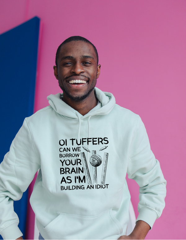 A man wearing a white hoodie with Oi Tuffers, can we borrow your brains as I'm building an idiot, on the front.  Funny Cricket Hoodie, Premium Fabric, Multiple Adult Sizes