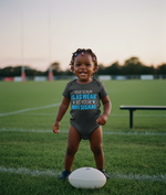 Child wearing a humorous t-shirt on a sports field. The baby is wearing a Cows Corner baby grow with a funny rugby slogan 'Your Scrum Is As Weak as Your WiFi Signal'. Cows Corner gifts are perfect for sport-mad fans, these gifts work brilliantly for birthdays, new baby celebrations, Father’s Day, Mother’s Day, Christmas, anniversaries, thank you gifts, end-of-season team awards, graduations, retirements, and just-because moments when you want to raise a smile. 
