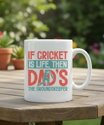 White mug with cricket-themed text on a wooden table outdoors. This is a Cows Corner mug with a funny cricket slogan 'If Cricket Is Life, Then Dad's The Groundkeeper'.  Cows Corner gifts are perfect for sport-mad fans, these gifts work brilliantly for birthdays, new baby celebrations, Father’s Day, Mother’s Day, Christmas, anniversaries, thank you gifts, end-of-season team awards, graduations, retirements, and just-because moments when you want to raise a smile. 
