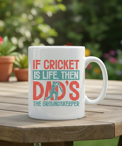 White mug with cricket-themed text on a wooden table outdoors. This is a Cows Corner mug with a funny cricket slogan 'If Cricket Is Life, Then Dad's The Groundkeeper'.  Cows Corner gifts are perfect for sport-mad fans, these gifts work brilliantly for birthdays, new baby celebrations, Father’s Day, Mother’s Day, Christmas, anniversaries, thank you gifts, end-of-season team awards, graduations, retirements, and just-because moments when you want to raise a smile. 
