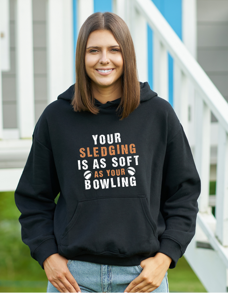 A lady wearing a black hoodie with Your Sledging Is as Soft as Your Bowling on the front.  A Funny Cricket Hoodie, Premium Fabric, Multiple Adult Sizes